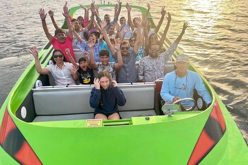 A group of people on a green boat with raised hands, on a body of water. 2