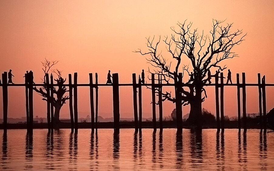Un atardecer sobre una masa de agua, con una valla de madera y árboles despojados de hojas silueteados contra el cielo. 5