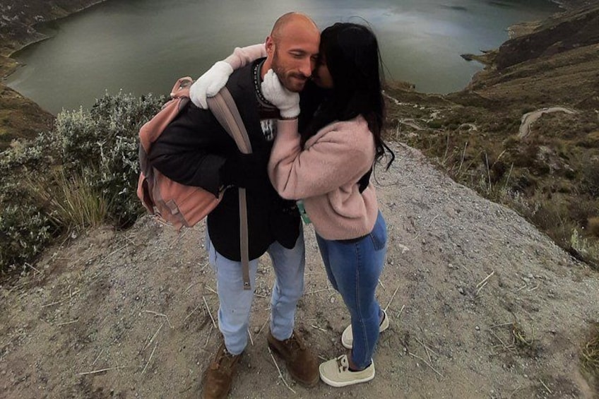 Two people embracing on a rocky hillside with a lake in the background. 1