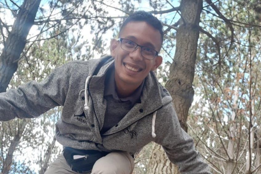 A person crouching in a forested area with trees and branches in the background. 5