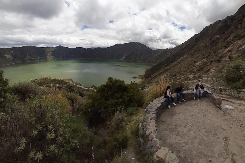 A group of people sitting on a stone bench overlooking a lake surrounded by mountains. 4