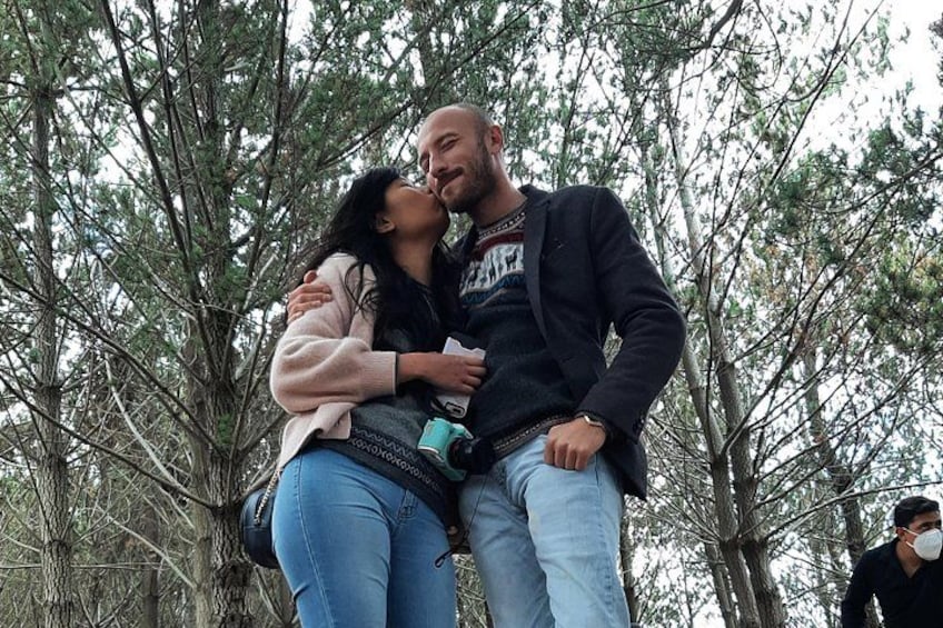 A couple embracing in a forested area with tall trees. 2