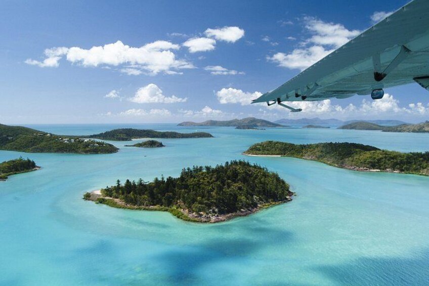 An aerial view of a turquoise sea with several small islands, one with dense green vegetation. 3