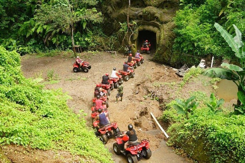A line of red quad bikes on a dirt path through a lush green forest. 1