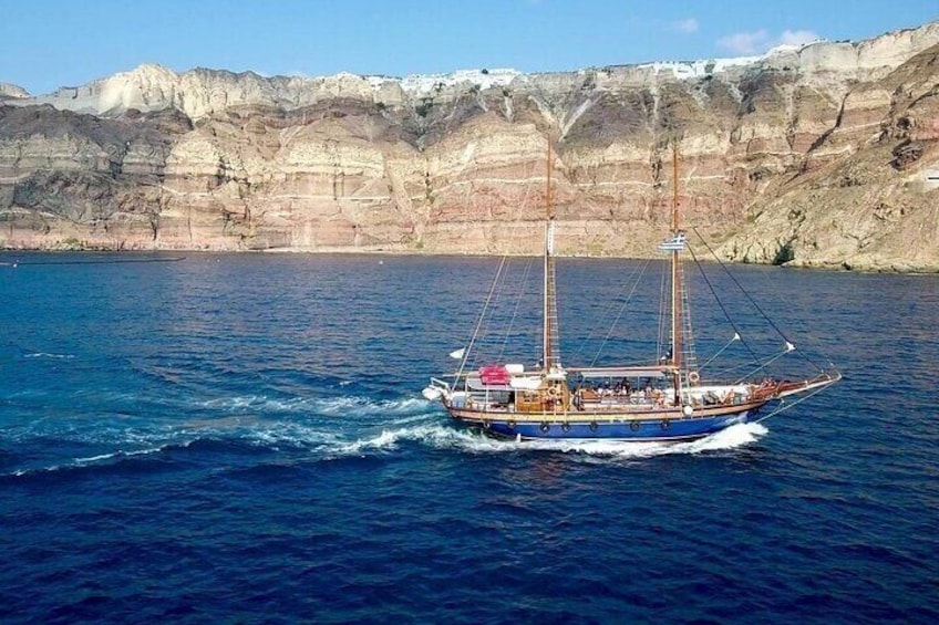 A sailing boat on a calm sea with cliffs in the background. 1