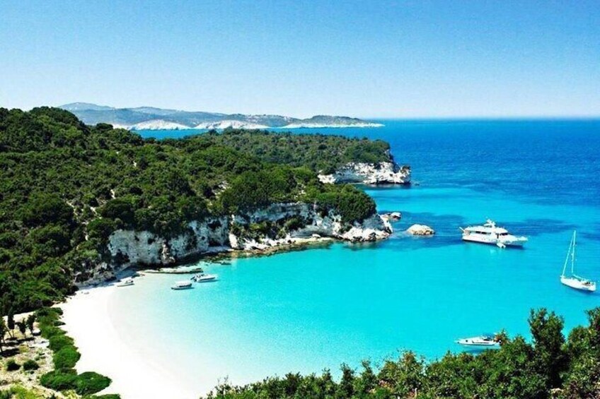 A coastal landscape with a clear blue sea, boats, and a white sandy beach. 1