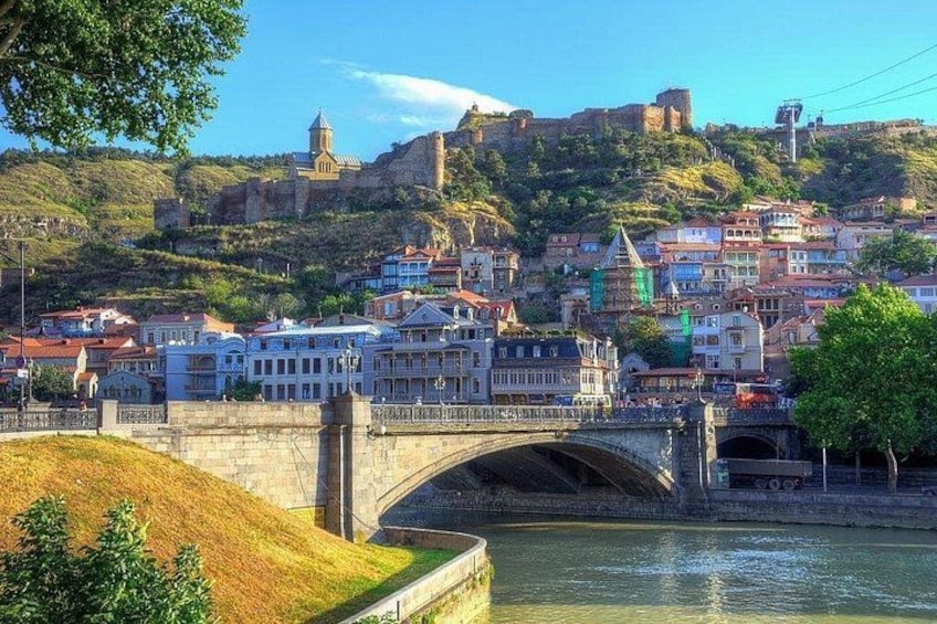 A bridge over a river, a historic castle on a hill, and a town with colorful buildings. 2