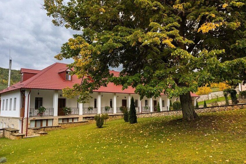 Une maison blanche avec un toit rouge, entourée d’un mur de pierre et d’un grand arbre aux feuilles jaunes. 5