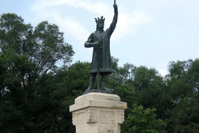 Una estatua sobre un pedestal con inscripciones, rodeada de árboles. 5
