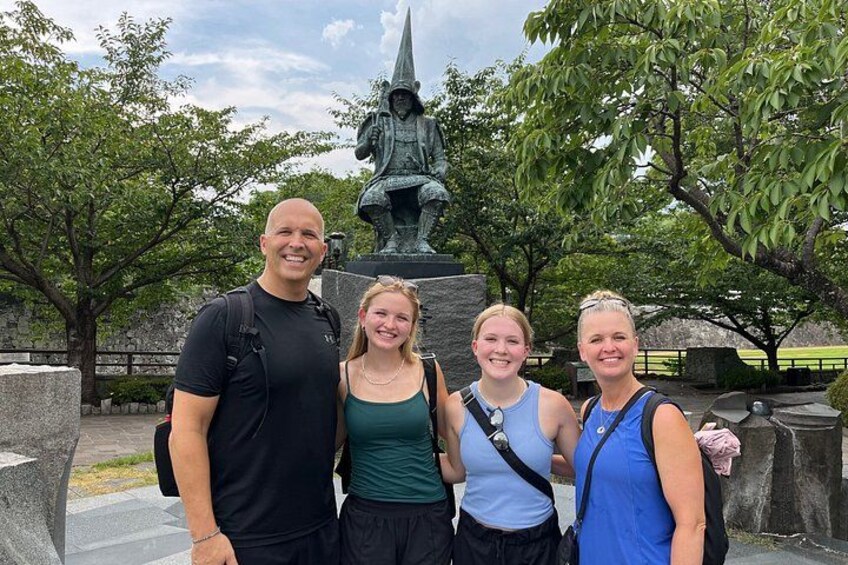 A group of people standing in front of a statue with a park in the background. 3