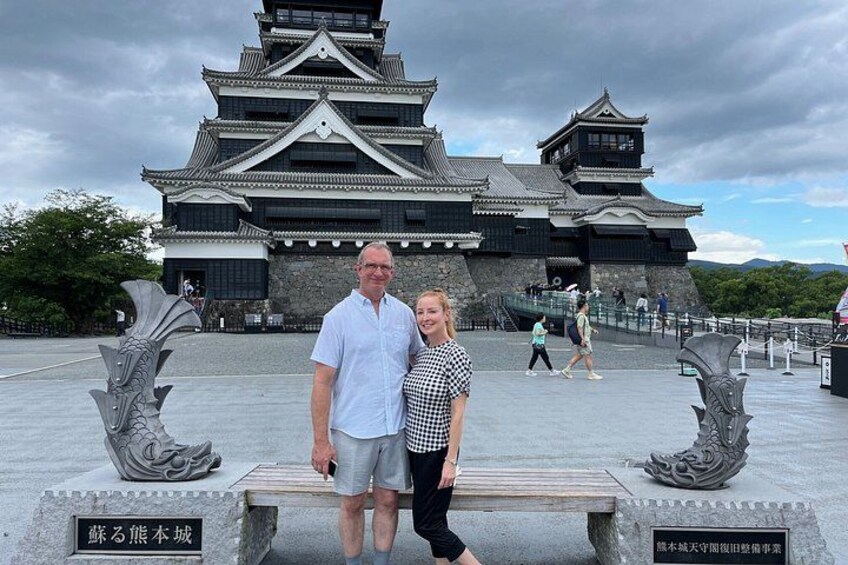 A castle with traditional architecture, a stone bench, and two people standing in front. 2
