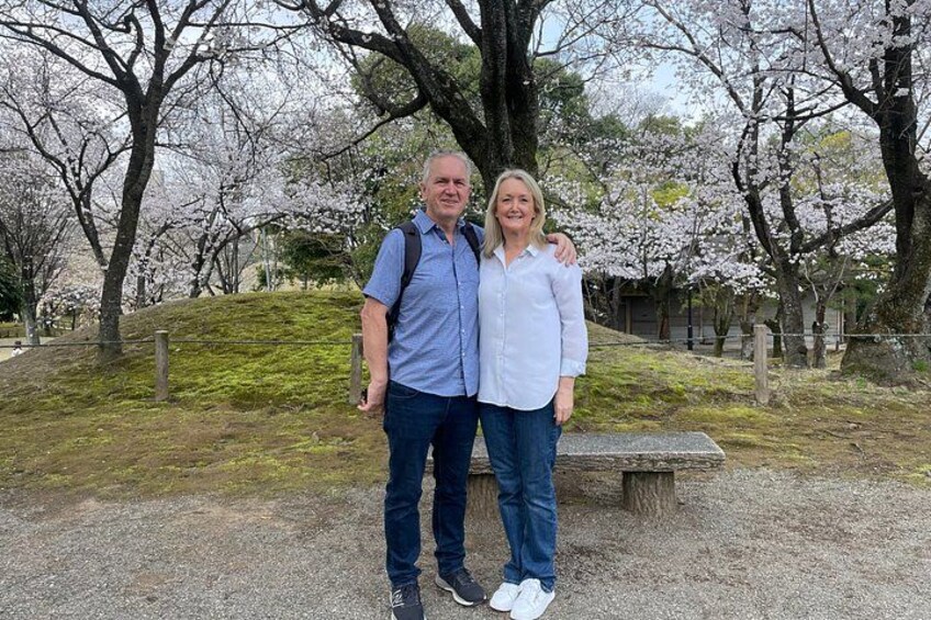 Two people standing in a park with cherry blossoms. 4