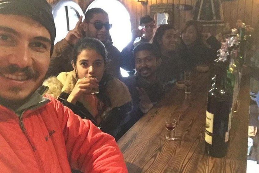 A group of people sitting at a wooden table with a bottle of wine and glasses. 3