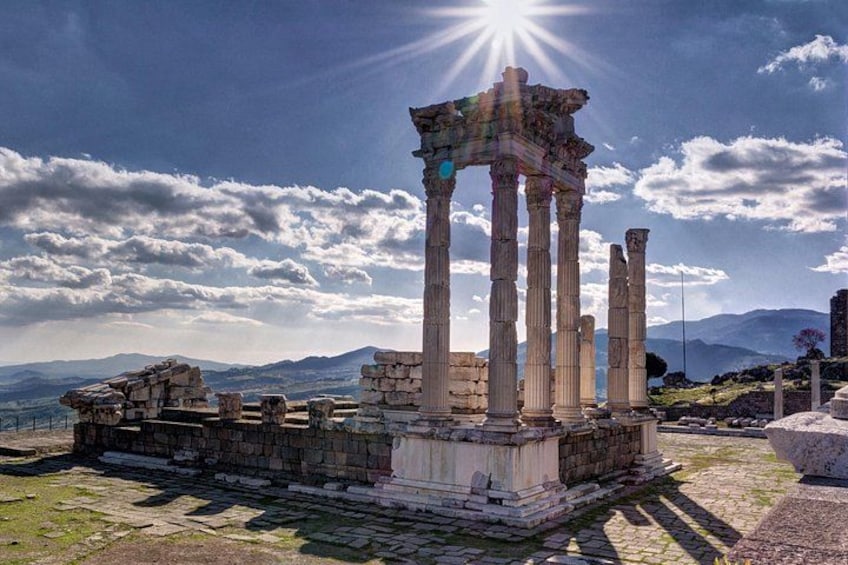 Ancient ruins with columns, a stone wall, and a mountainous landscape under a clear sky. 1