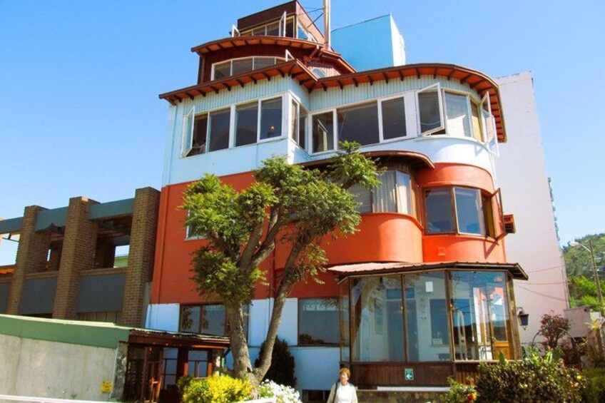 A multi-story building with a red and white facade, a balcony, and a tree in the foreground. 4