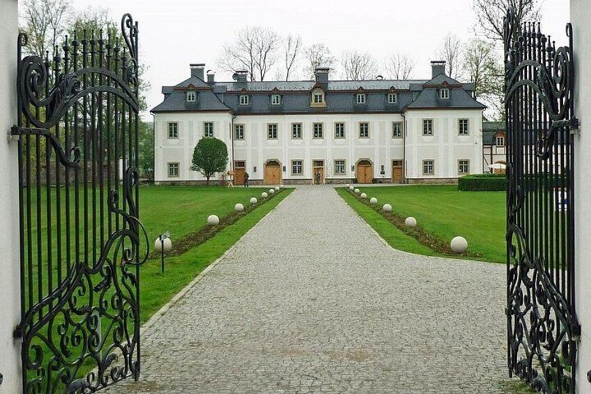 A large white building with a symmetrical facade, a paved driveway, and a gated entrance. 3