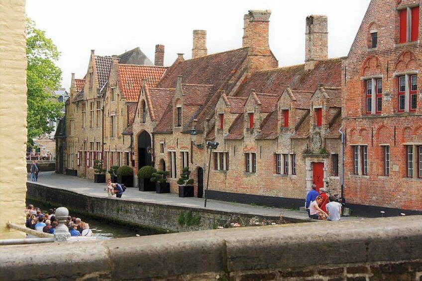 A canal with people sitting on the edge, historic buildings with red roofs, and a bridge in the background. 5