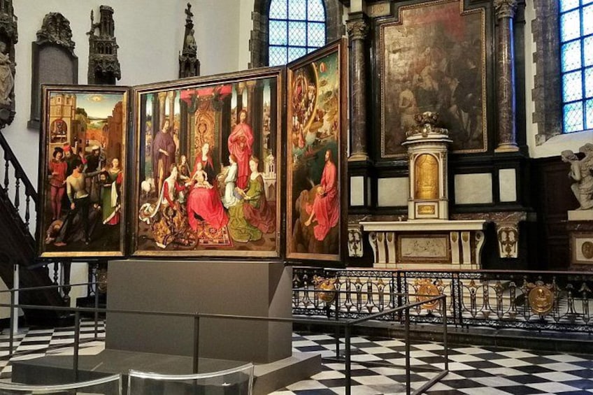 A church interior with a large triptych painting, a wooden altar, and a checkered floor. 1