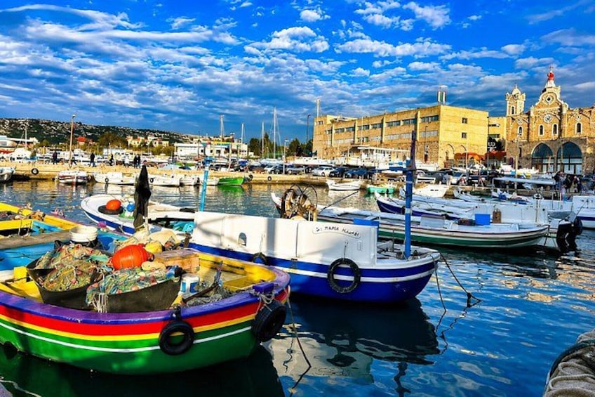 Un port où flottent des bateaux aux couleurs vives, un grand bâtiment surmonté d’une tour horlogère et un ciel d’un bleu limpide. 4