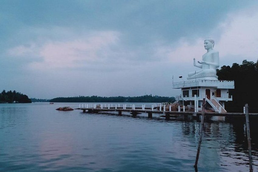 A large white statue on a platform by a calm body of water, with a dock extending into the water. 5