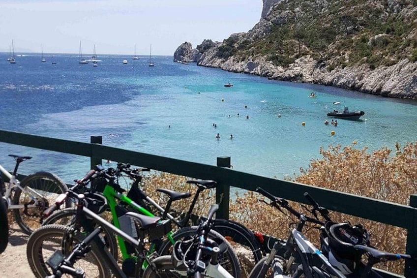 A coastal area with bicycles parked in the foreground, a rocky shoreline, and sailboats in the water. 2