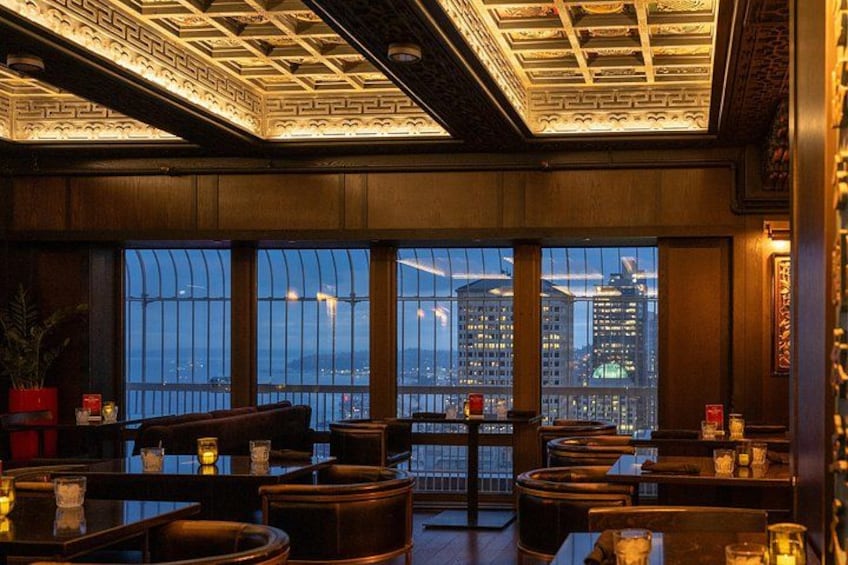 Un restaurant avec des tables et des chaises, de grandes fenêtres offrant une vue sur le paysage urbain et un plafond décoratif. 3