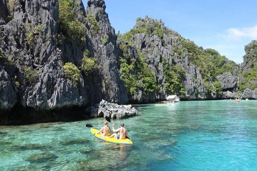 A kayak on clear turquoise water, rocky cliffs, and a boat in the background. 4
