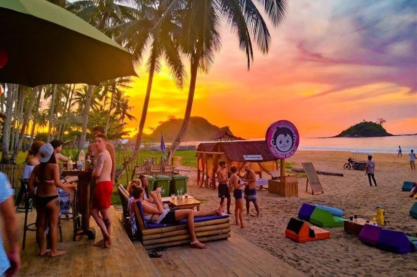 A beach scene with people relaxing on lounge chairs, a wooden deck, and palm trees. 2