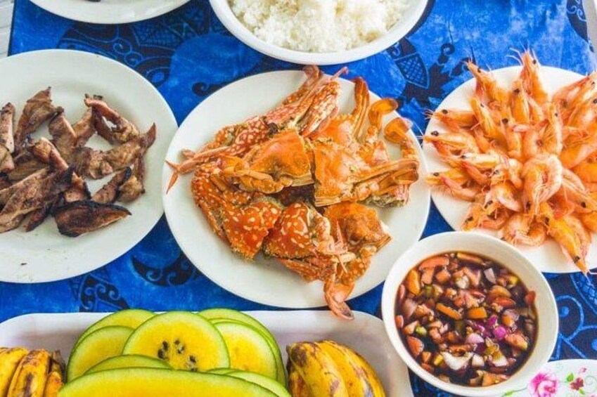 A variety of seafood dishes including grilled shrimp, crab, and sliced bananas on a blue tablecloth. 5
