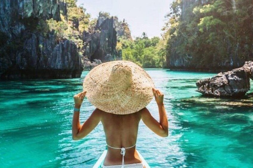 A person in a boat wearing a straw hat, surrounded by clear turquoise water and rocky cliffs. 1