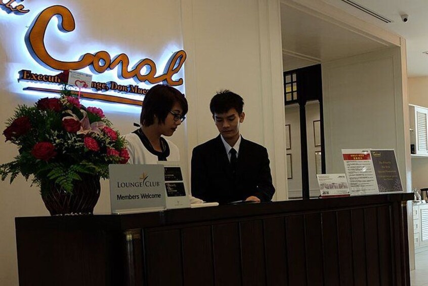 En receptionsdisk med et skilt, der siger 'Lounge Club Members Welcome', og en blomsterdekoration. 2