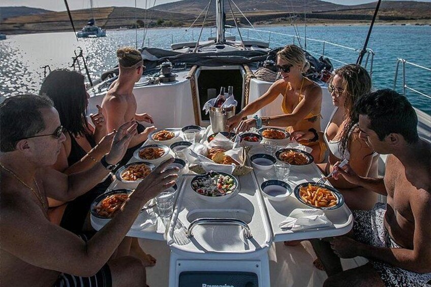 En grupp människor som äter middag på en båt, med ett dukat bord, omgivna av vatten och andra båtar i bakgrunden. 2