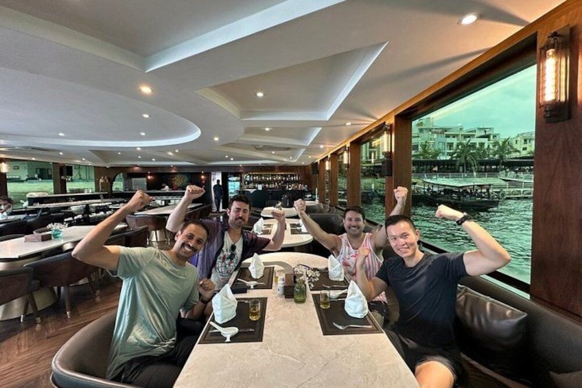 Un grupo de personas sentadas en una mesa en un restaurante, con vistas a un cuerpo de agua y edificios al fondo. 3