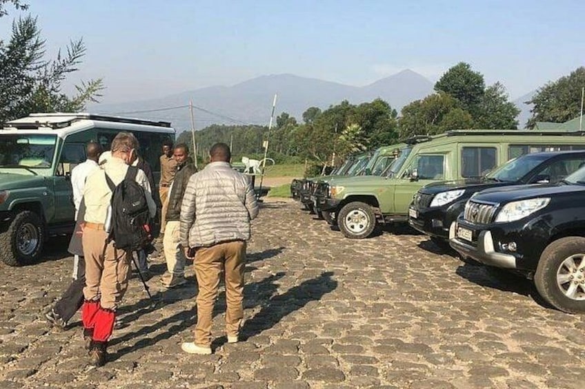 A group of people standing in front of a row of vehicles on a cobblestone path with mountains in the background. 4