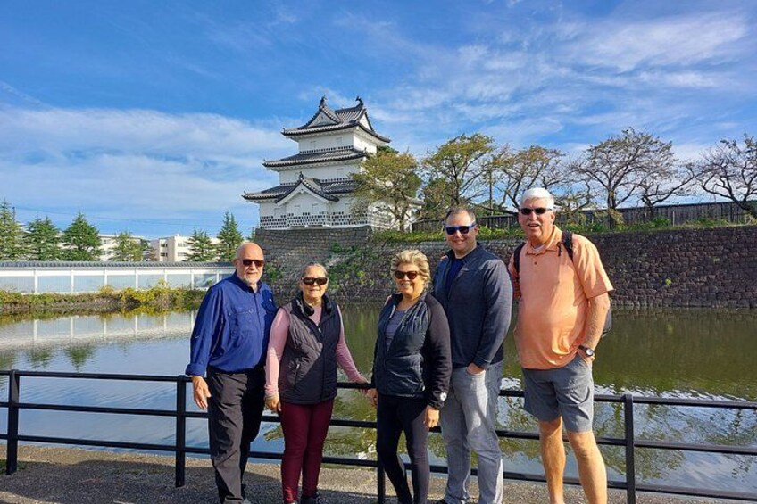Eine Gruppe von Personen steht vor einer traditionellen japanischen Burg, im Hintergrund ist ein Burggraben zu sehen. 5