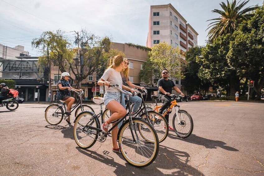 Three people riding bicycles on a city street with buildings and palm trees in the background. 4