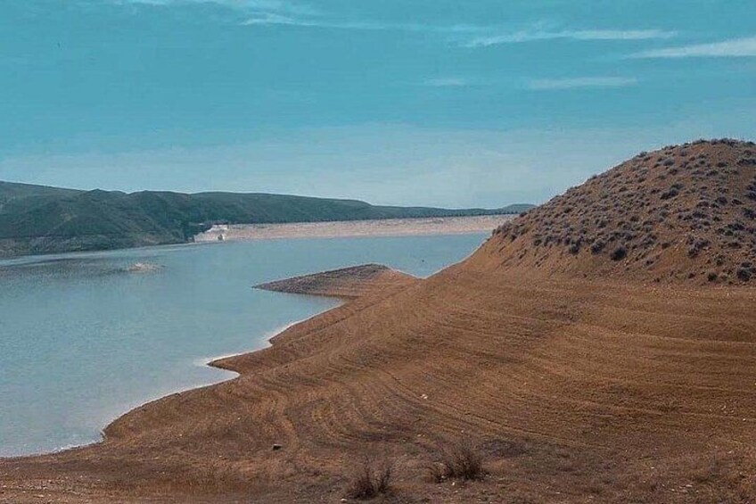 A dry lakebed with a small body of water, a hill, and distant hills. 1