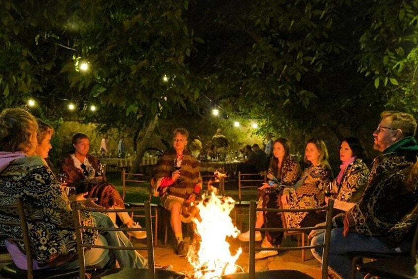 A group of people sitting around a campfire outdoors at night. 2