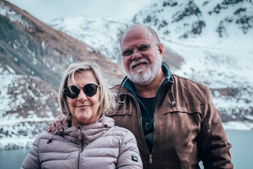 Two people standing by a body of water with snow-covered mountains in the background. 5