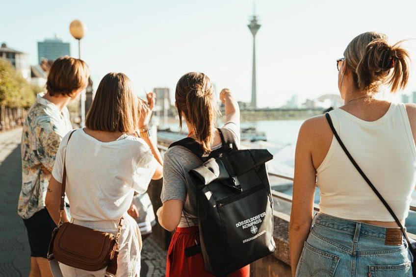 A group of people walking along a waterfront with a tower in the background. 3