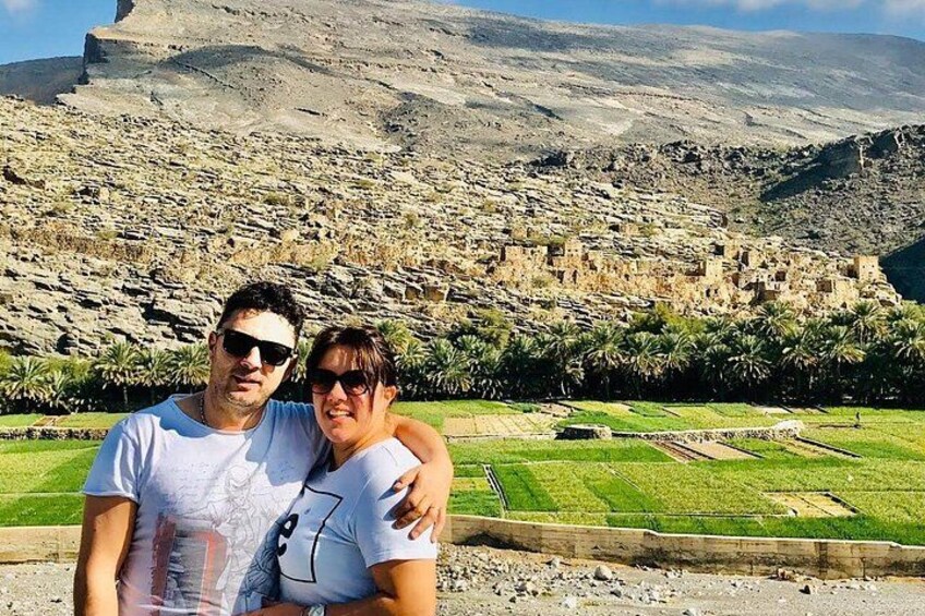 Two people standing in front of a historical site with ruins and green fields. 1
