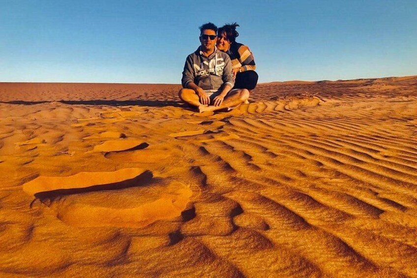 Two people sitting on a sand dune in a desert. 4