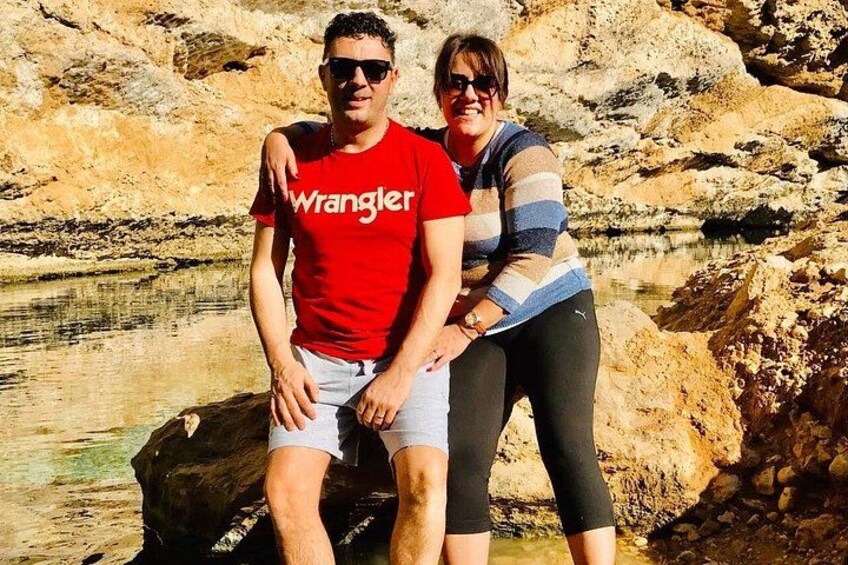 Two people sitting on a rock by a body of water with a rocky shoreline in the background. 3