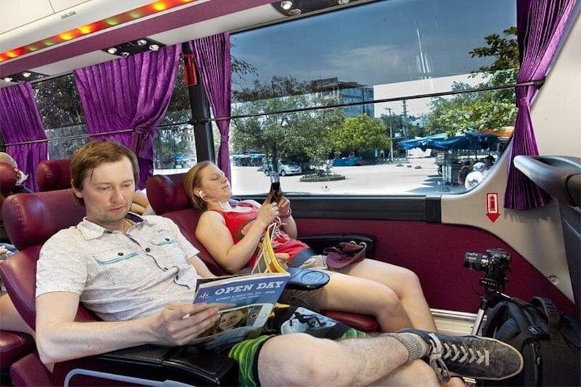 A bus interior with purple curtains, passengers seated, and a window view of a parking lot. 2