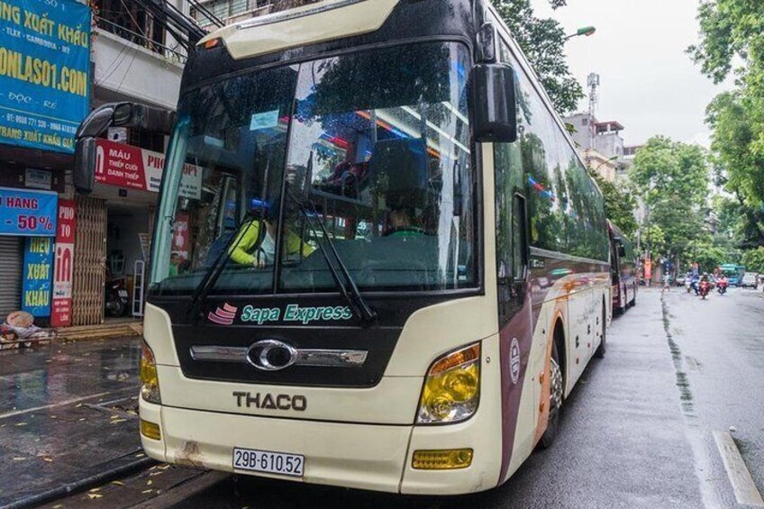 A THACO bus with 'Sapa Express' branding parked on a wet street. 1