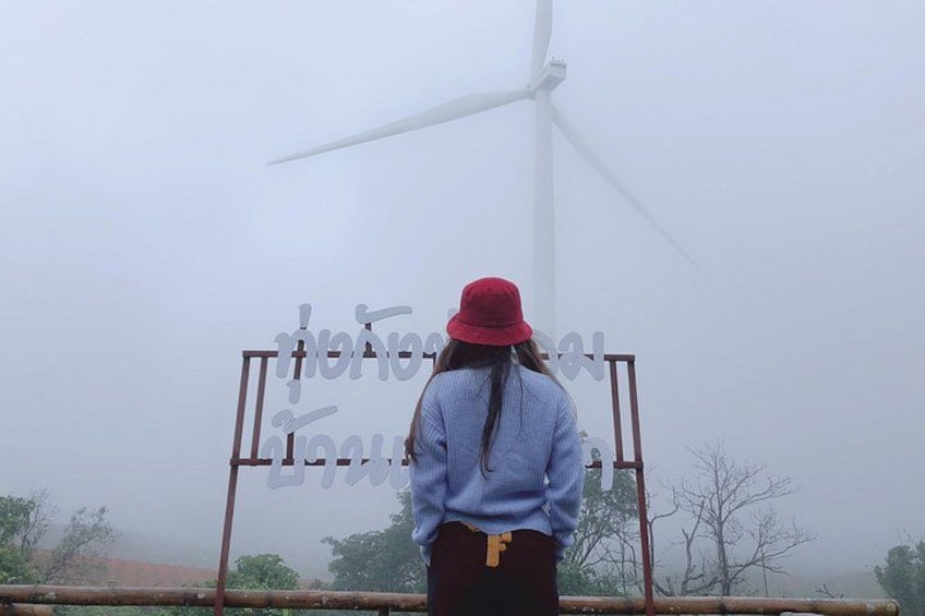 A person standing in front of a wind turbine with a sign in the background. 1