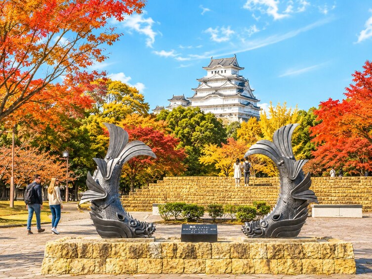 En park med höstfärgat lövverk, ett traditionellt japanskt slott och två drakonskulpturer. 1