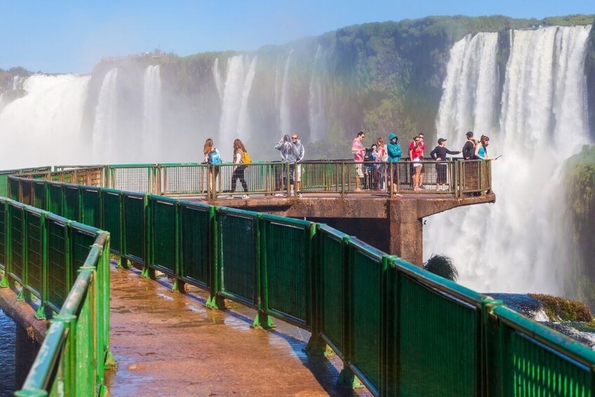 A group of people standing on a bridge overlooking a large waterfall. 3