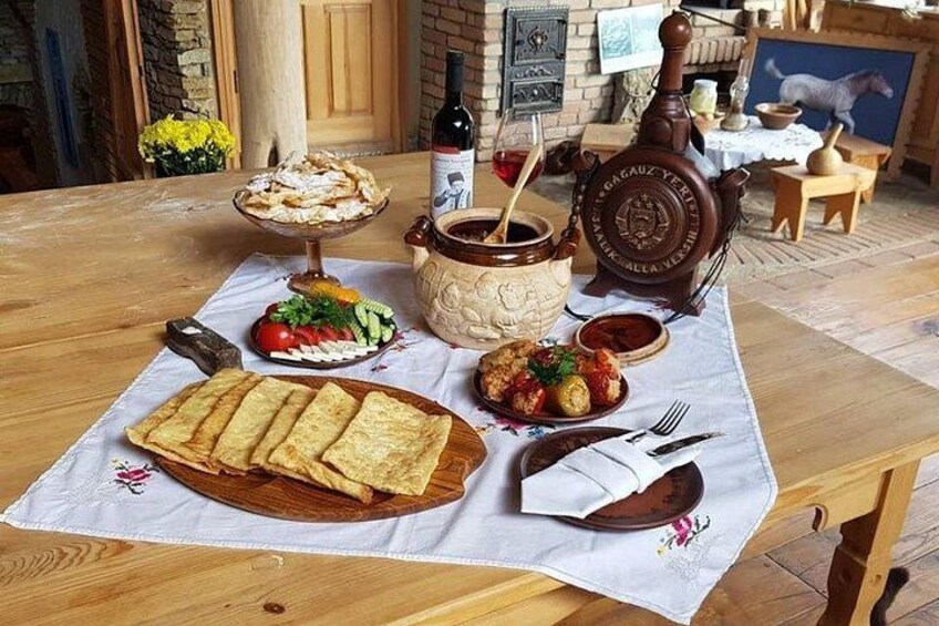 Een houten tafel met diverse gerechten, waaronder brood, salade en een soepterrine. 1