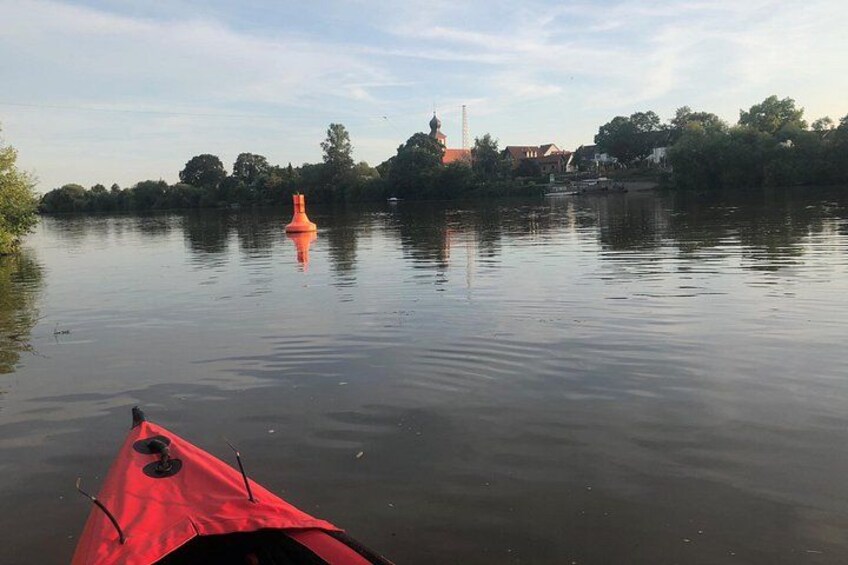 Un lago tranquilo con un kayak rojo al frente y la aguja de una iglesia en el fondo. 3